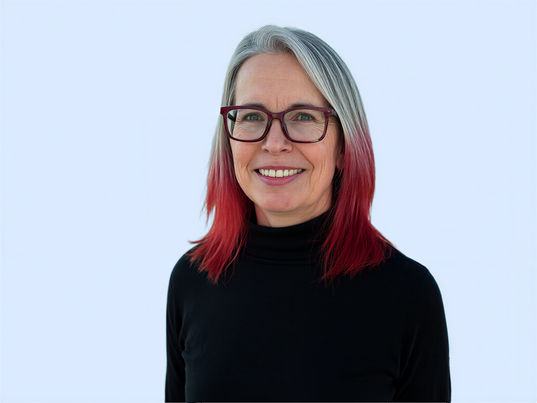 Woman with gray hair and red ends wearing red glasses and a black shirt and smiling